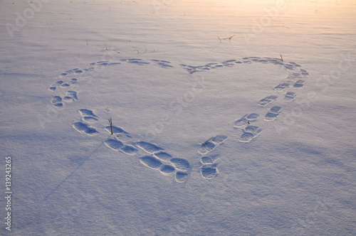 Snowy field with shoe imprints in the shape of a heart in winter.