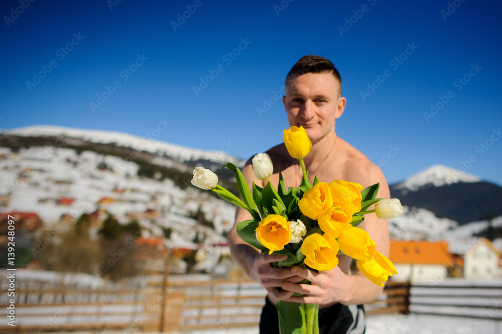 Fototapeta premium Young man with a bouquet against the background of snow-covered mountains.