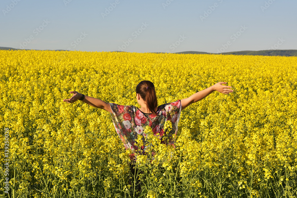 Fototapeta premium Young happy woman on blooming rapeseed field in spring