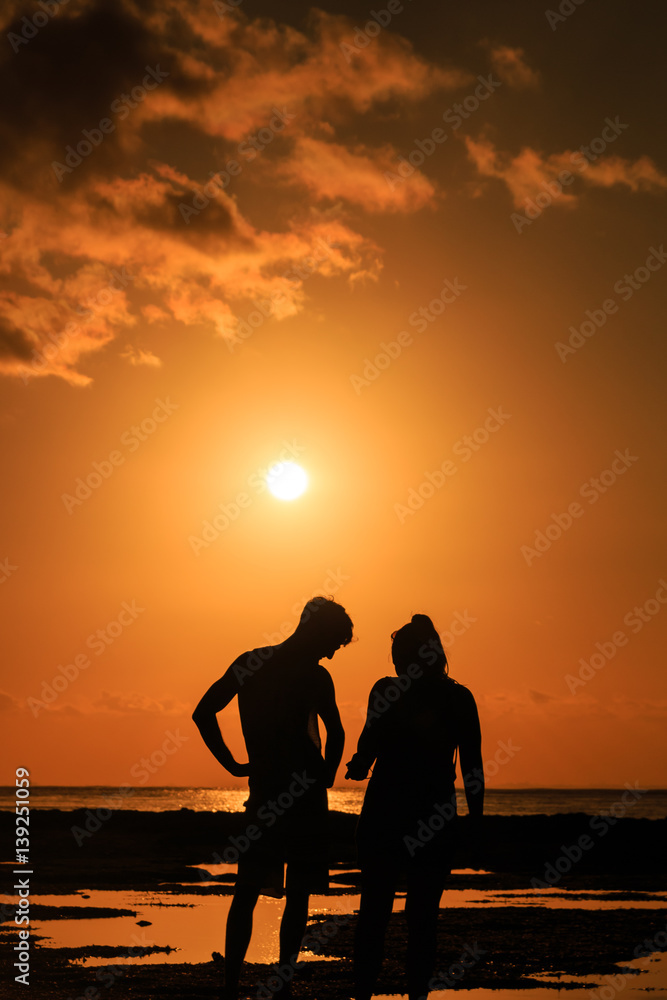 A couple watching sunset over a tropical ocean