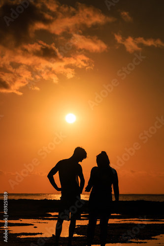 A couple watching sunset over a tropical ocean
