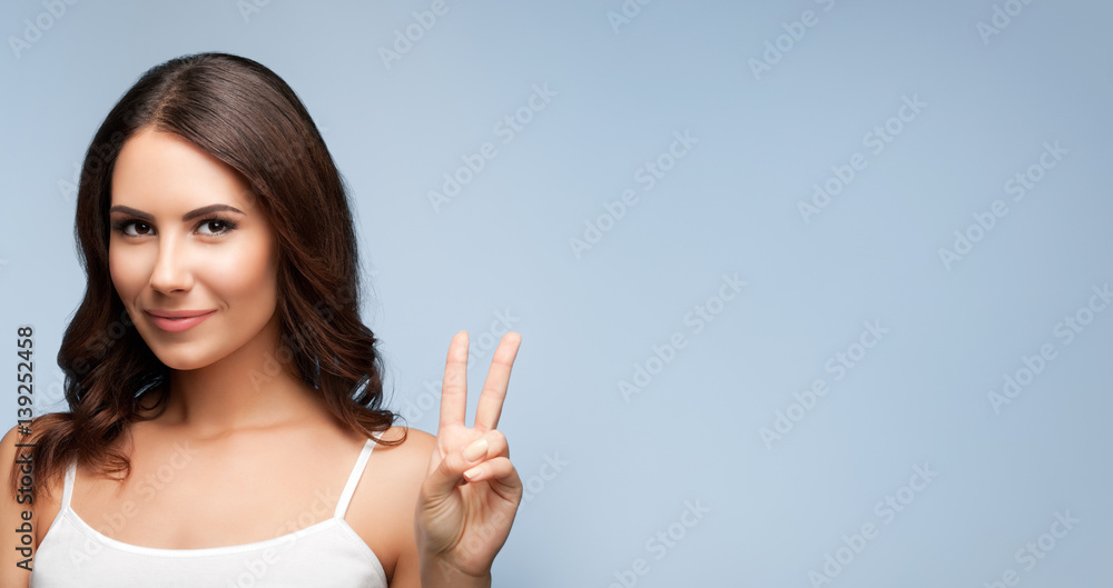 Woman showing two fingers or victory gesture, on grey Woman showing two fingers or victory gesture, on grey