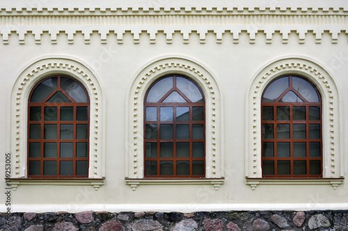 Three brown old arched windows on a white wall plaster.