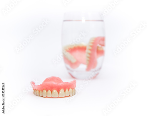 Acrylic dentures immersed in a glass of water,white background.
