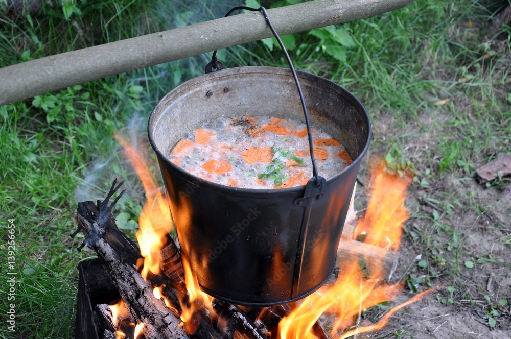 The process of cooking in the campaign. Metal bucket of fish soup on the fire. The process of cooking in the campaign. Metal bucket of fish soup on the fire.