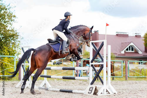Young horseback sportswoman jumping over obstacles on show jumping competition © skumer