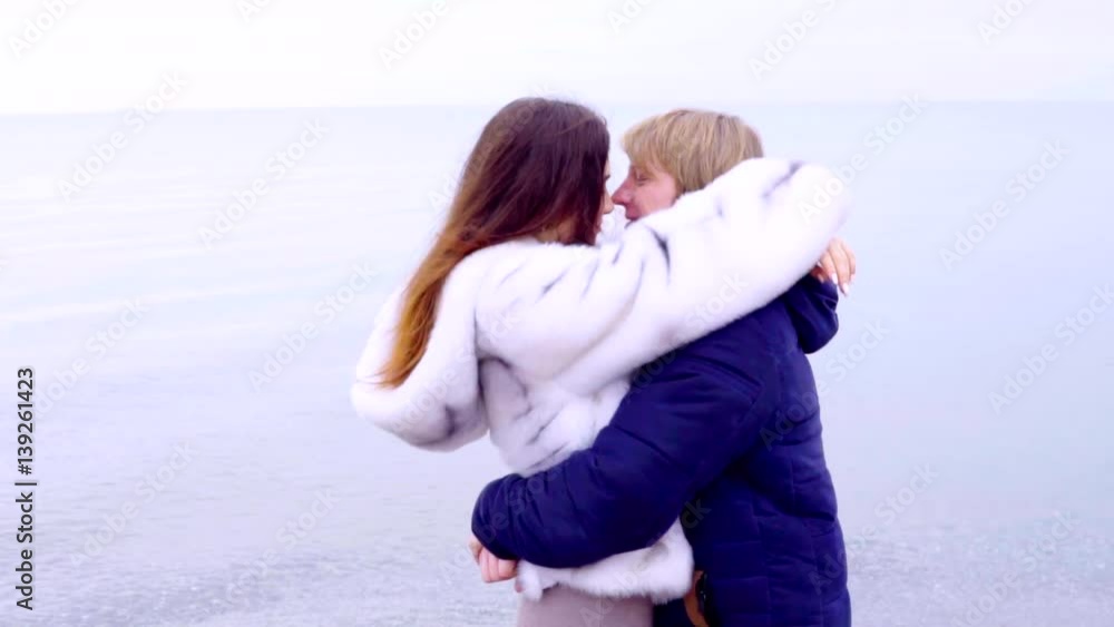 Couple embracing one another on the beach joyful wearing warm coats on the sand beach. Woman and man model enjoying nature landscape at the sea. Couple embracing one another on the beach joyful wearing warm coats on the sand beach. Woman and man model enjoying nature landscape at the sea.