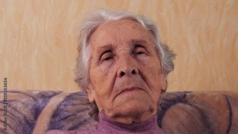 Elderly woman blinking. A woman at the age sitting on the couch. Face