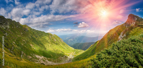 Panoramic landscape of summer mountains. View of cliff tops and green hills at sunlight. 