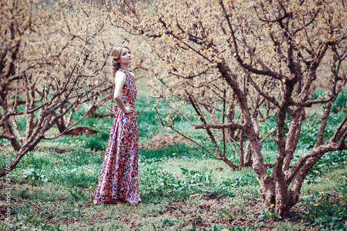 Portrait of a young blond woman in a pink dress on a background of flowering trees