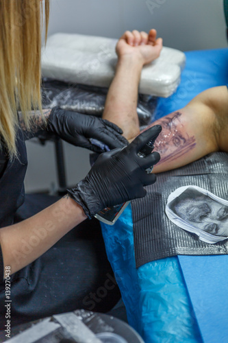 A blonde tattooist portrays a tattoo on a boy´s arm