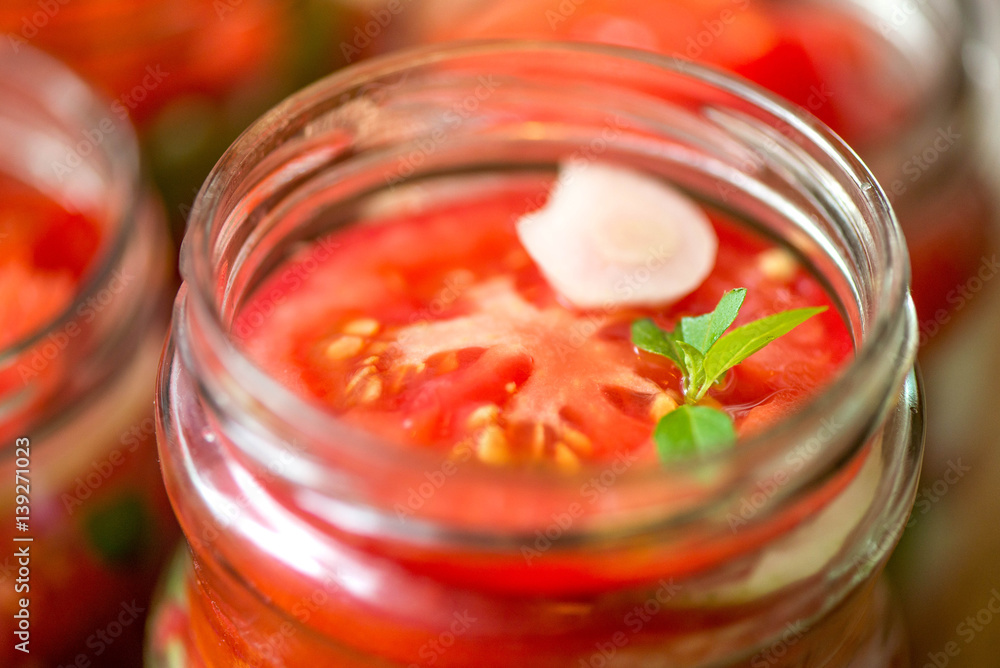 Canning fresh tomatoes with onions for winter in jelly marinade. Macro shot of basil leaves on top of a red ripe tomato slice being put in jar.
Canning fresh tomatoes with onions for winter in jelly marinade. Macro shot of basil leaves on top of a red ripe tomato slice being put in jar.
