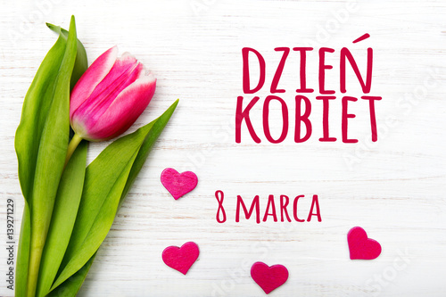Women's day card with Polish words DZIEŃ KOBIET. Tulip flower small hearts on white wooden background.
