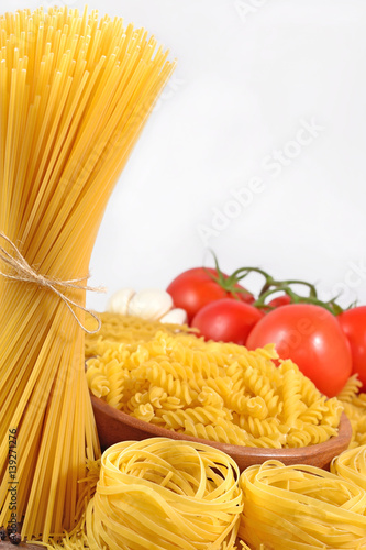 Uncooked Italian pasta and ripe tomatoes branch on a white