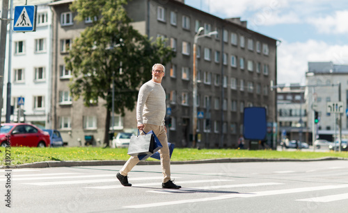 senior man with shopping bags walking on crosswalk