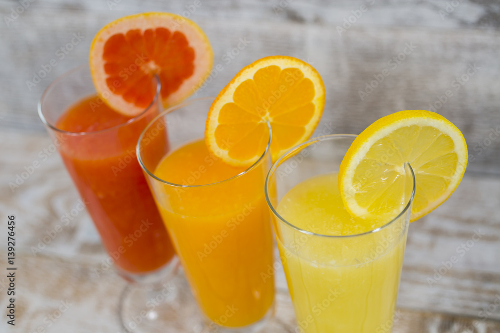 Citrus juices in glass and a slice of lemon, grapefruit and orange on wooden background . Citrus juices in glass and a slice of lemon, grapefruit and orange on wooden background .