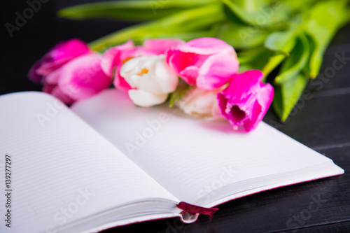 Fototapeta Naklejka Na Ścianę i Meble -  Bouquet of tender pink tulips and open notebook on black wooden background