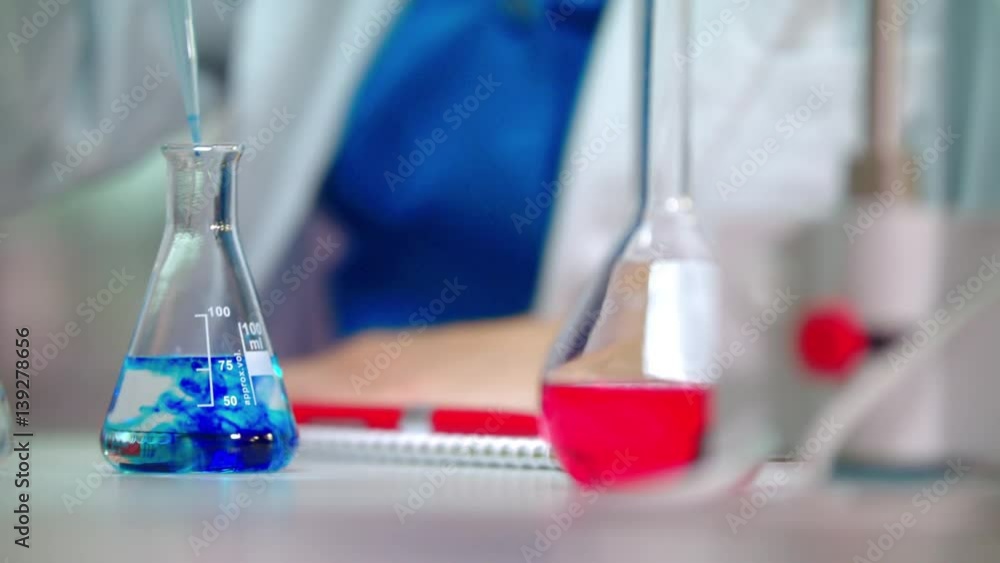 Clinical testing. Lab experiment in glass flask. Pouring blue reagent in pure solution. Closeup of chemical reaction in lab flask. Laboratory research. Lab research in lab flask. Chemical analysis Clinical testing. Lab experiment in glass flask. Pouring blue reagent in pure solution. Closeup of chemical reaction in lab flask. Laboratory research. Lab research in lab flask. Chemical analysis