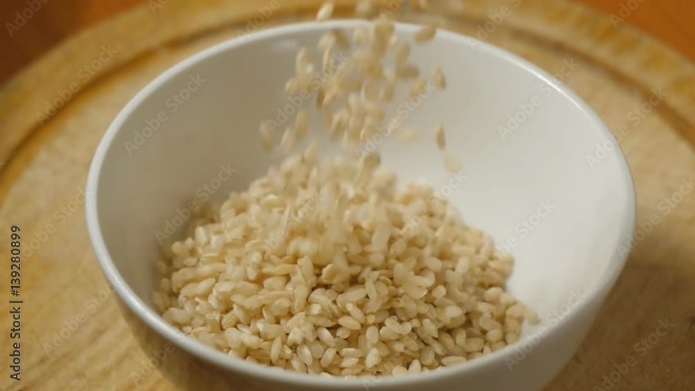 Whole rice grains falling in white ceramic bowl Whole rice grains falling in white ceramic bowl