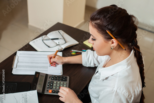 Young female bookkeeper considers on calculator photo