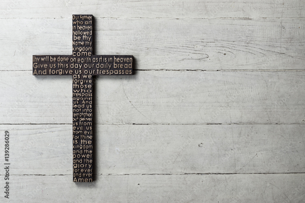 Dark wooden cross with carved the Lord's Prayer on worn white wooden background