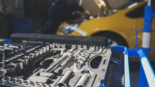 Mechanic repairs yellow car in professional auto service, de-focused