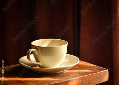 Empty coffee cup under afternoon sunlight prepared for coffee time. Dark room corner background.