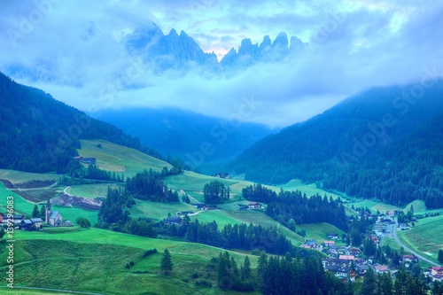 Beautiful scenery of majestic Puez Odle or Geisler Mountain Peaks in Val di Funes with view of Santa Maddalena  Magdalena  village in the green grassy valley in Dolomites  South Tyrol  Italy  Europe