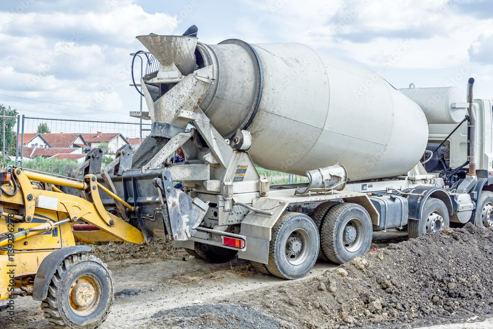 Truck mixer in process of pouring concrete into bulldozer scoop
