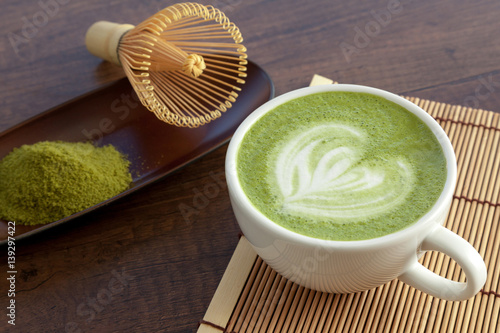 Matcha latte art heart shape on top on wooden table with some green tea powder beside and tools for tea making, Japanese style