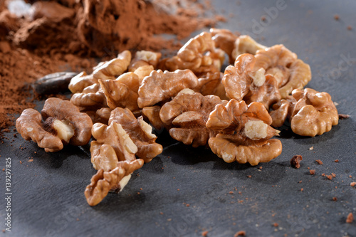 peeled walnuts kernels with cacao powder close-up on black slate plate 