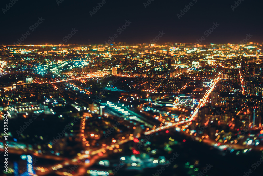 True tilt shift shooting of highway, railway and residential district in night metropolis from high point: multiple residential houses in focus in the middle, strong bokeh in background and foreground