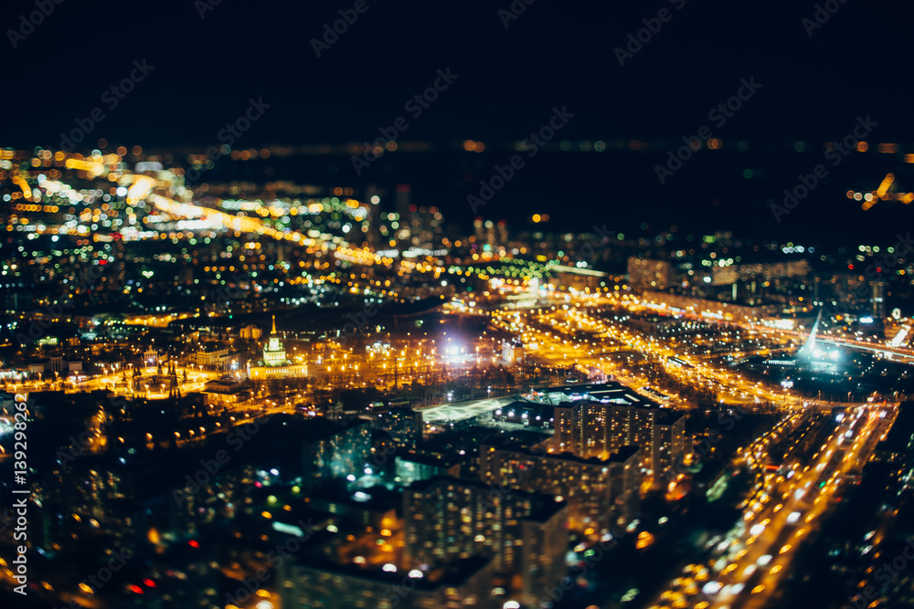 Fototapeta premium True tilt shift shooting of VDNKh district of night Moscow from very high point: multiple buildings, main street of VDNKh in focus, strong bokeh in foreground and background, square with monument