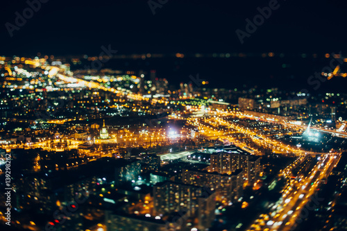 True tilt shift shooting of VDNKh district of night Moscow from very high point: multiple buildings, main street of VDNKh in focus, strong bokeh in foreground and background, square with monument