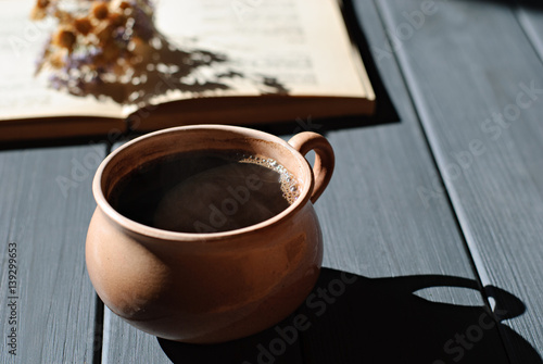 Cup of coffee, dry flowers and open book on wooden table. Romantic and retro background, hard light