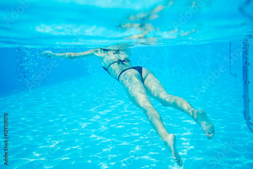 Woman in black bikini floating at swimming pool, photo underwater, copy space