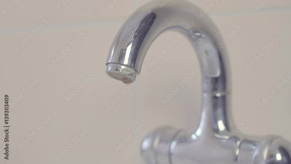 dripping bathroom faucet spout. View from front straight on at low angle dripping bathroom faucet spout. View from front straight on at low angle