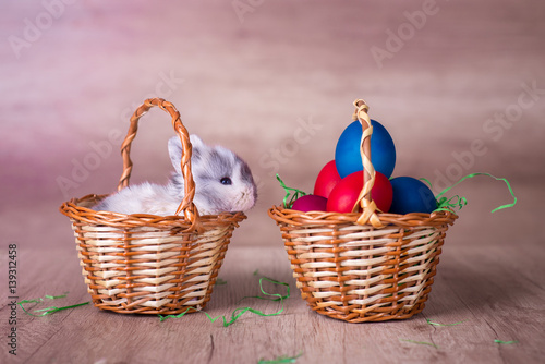 Happy easter, bunny in a basket with a basket of colorful easter eggs next to it