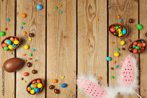 Easter holiday concept with chocolate eggs and bunny ears on wooden background. Top view from above with copy space