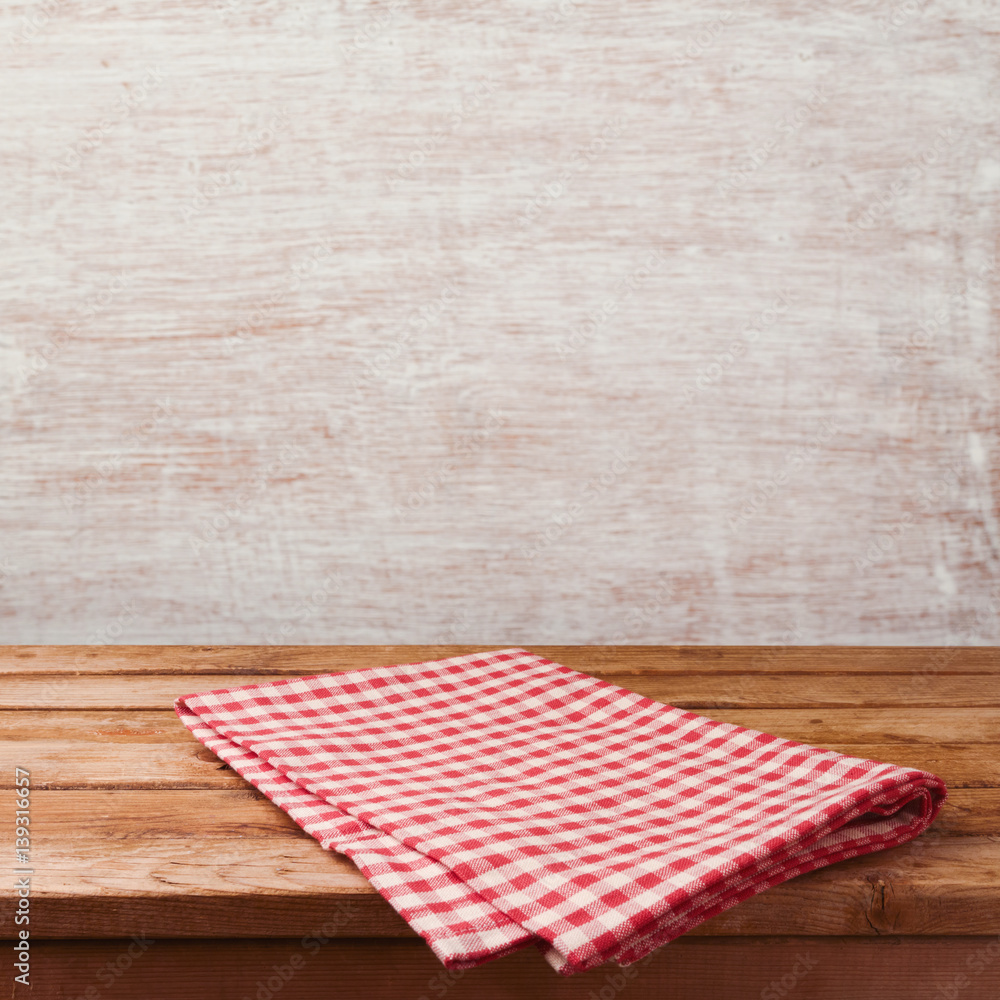 Empty wooden deck table with red cheched tablecloth over rustic wall background for product montage display. Restaurant or kitchen interior