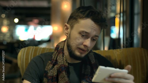 Man look tired while sitting in the dark cafe and browsing internet on smartphone
