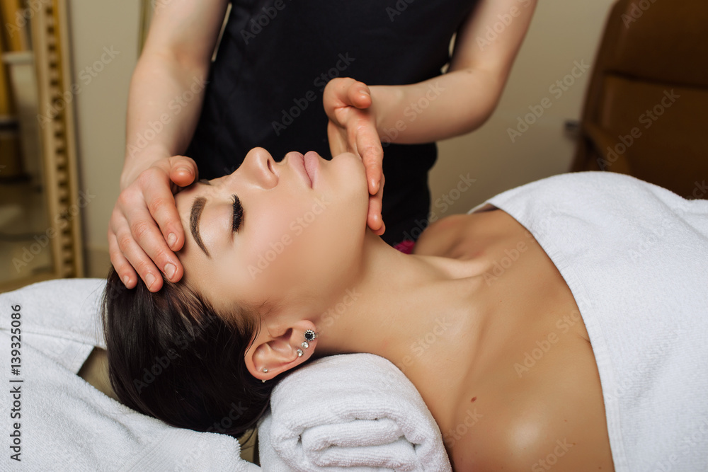 woman with closed eyes receiving face massage lying on a massage table,  massage therapist hands working on massaging woman's neck and chin.  Rejuvenating facial contour massage Stock Photo | Adobe Stock