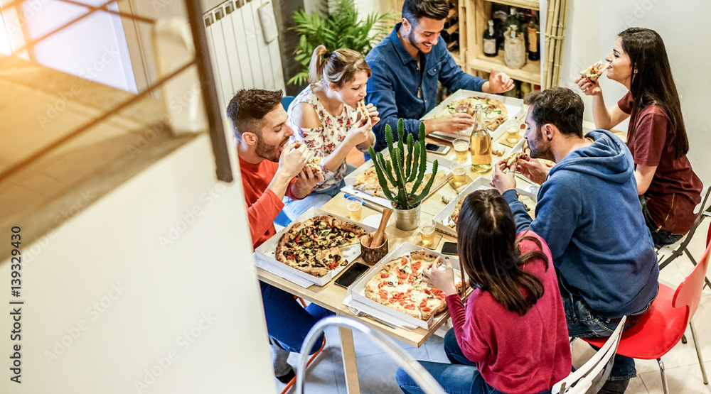 Obraz premium Loft view of happy friends eating pizza and toasting beer at home