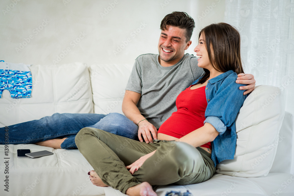 Happy couple with pregnant woman playing around sitting on sofa at home