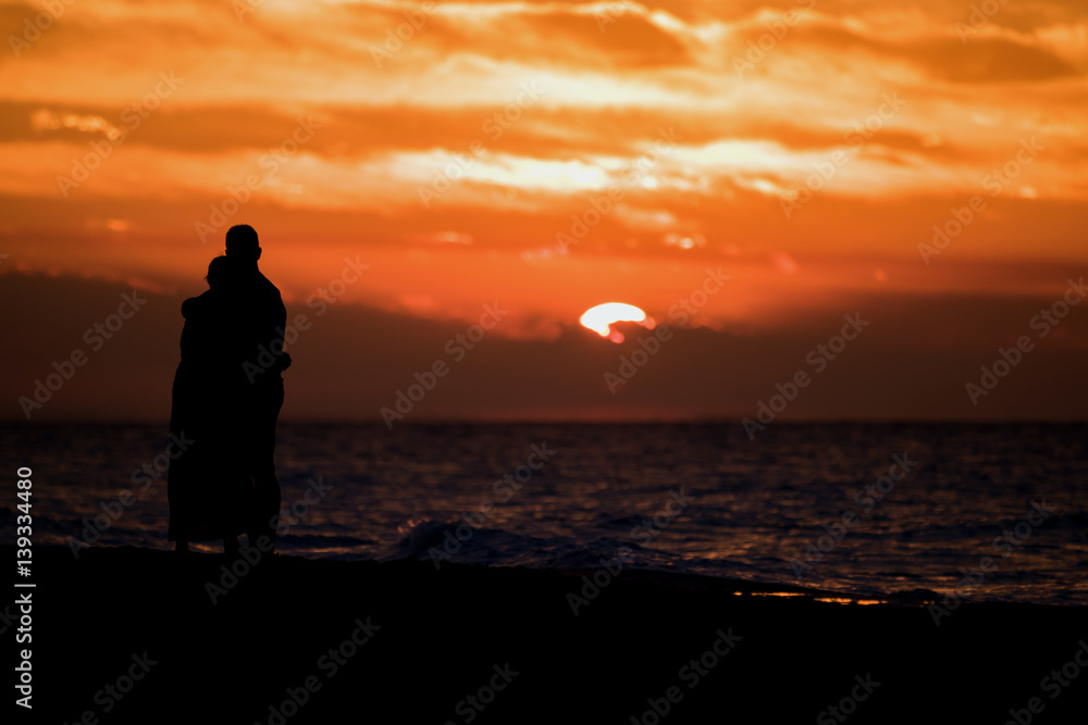 Paar am Strand bei wolkigem Sonnenuntergang