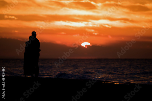 Paar am Strand bei wolkigem Sonnenuntergang