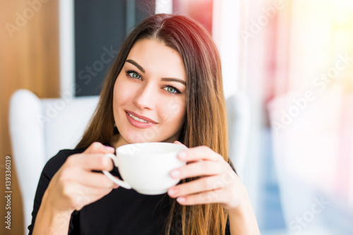 beautiful young woman drinking coffee or tea and look at camera