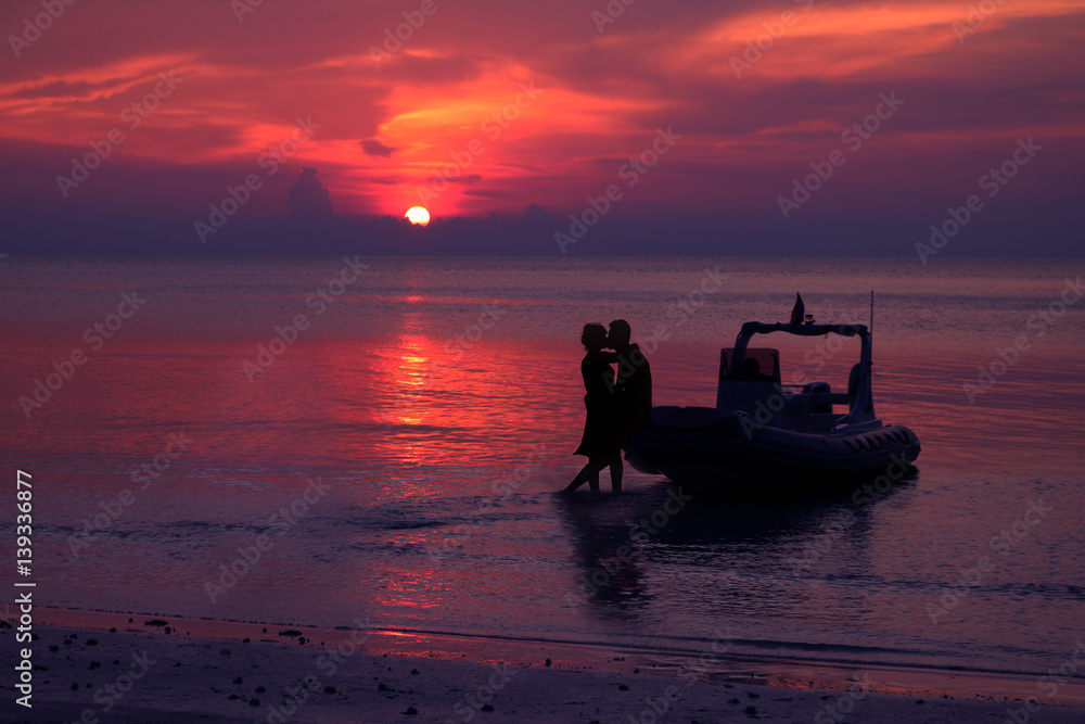 Silhouette couple kissing on the beach with dinghies private boat and purple sky sunset background 