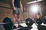 Sportive strong people standing at heavy barbells