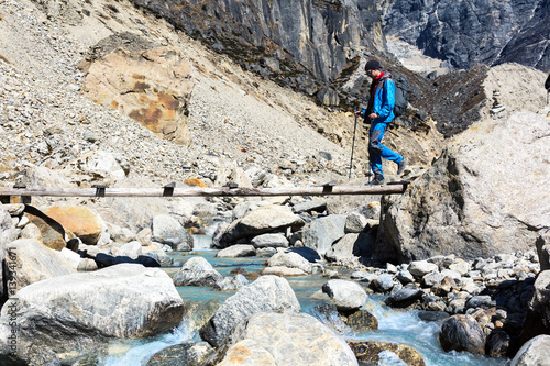 Hiker crossing Mountain River throw wooden Bridge